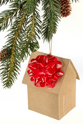 Brown Paper house ornament with red bow hanging from Christmas tree branch on white background. Vertical image would be good for Christmas use. Click to see other Christmas images..