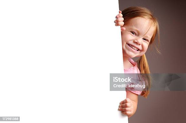 Rapariga Feliz Espreitar Por Detrás Sinal Em Branco - Fotografias de stock e mais imagens de Criança