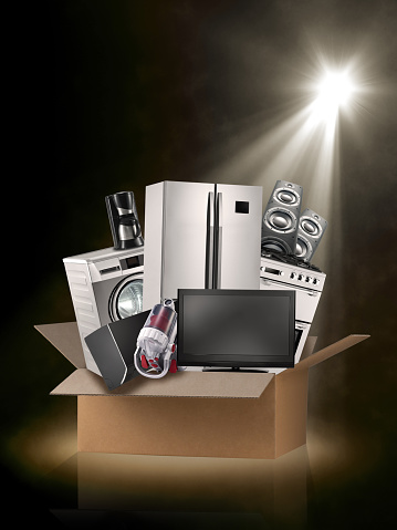 Spot lit home appliance set and electronic equipment inside a delivery box on a stage background