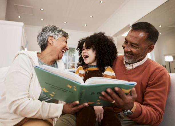 istock Grandparents, kid and laugh for reading, book or home for support, learning or education with love. Senior man, woman and happy child for funny story, teaching or help for development in family house 1729817796