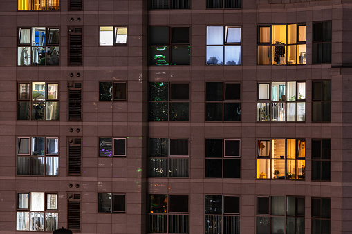 An apartment where houses with the same spatial structure are stacked like tiles. After sunset, lights turn on in the windows, showing different colored lights and furniture arrangements.