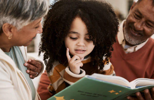 istock Grandparents, child and reading with book, home and thinking with support, learning and education. Senior man, woman and young kid with story, teaching and helping for development in family house 1729818105