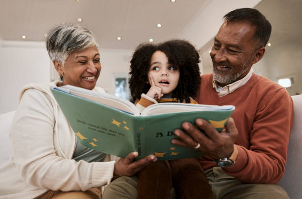 istock Grandparents, child and reading with book, sofa and thinking with support, learning and education. Senior man, woman and young kid with story, teaching and helping with development in family house 1729818657
