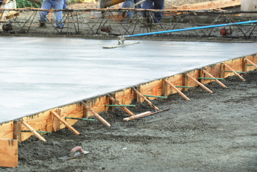Masonry construction workers smooth freshly poured concrete using bullfloat tool.