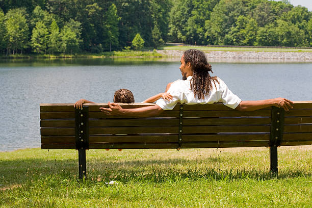 Rear view of father and son together on a park bench at lakeside