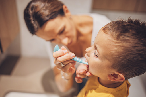 Mother brushing her little son teeth in domestic bathroom.