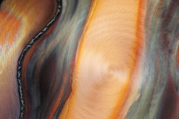 Funky abstract art design on circular brushed steel metallic disk.  A small section of sheet steel with coloring from intense heat and cirular scratch marks from a grinder create an interesting colorful abstract background.