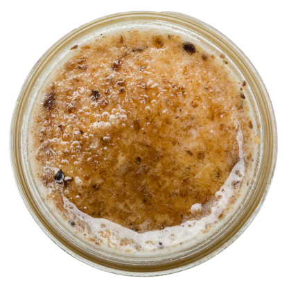 Top view of a jar of raw, unfiltered honey. Because it is unfiltered, the surface is covered with a layer of wax and cappings (this is normal for unfiltered honey). There is a little honey on the top of the wax & cappings layer. Isolated on a pure white background. Shallow DoF. 