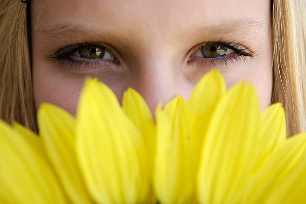 Fourteen-year-old girl with pretty hazel eyes peeks from behind a large sunflower. Focus is on her eyes. Please view my many other child and sunflower images.