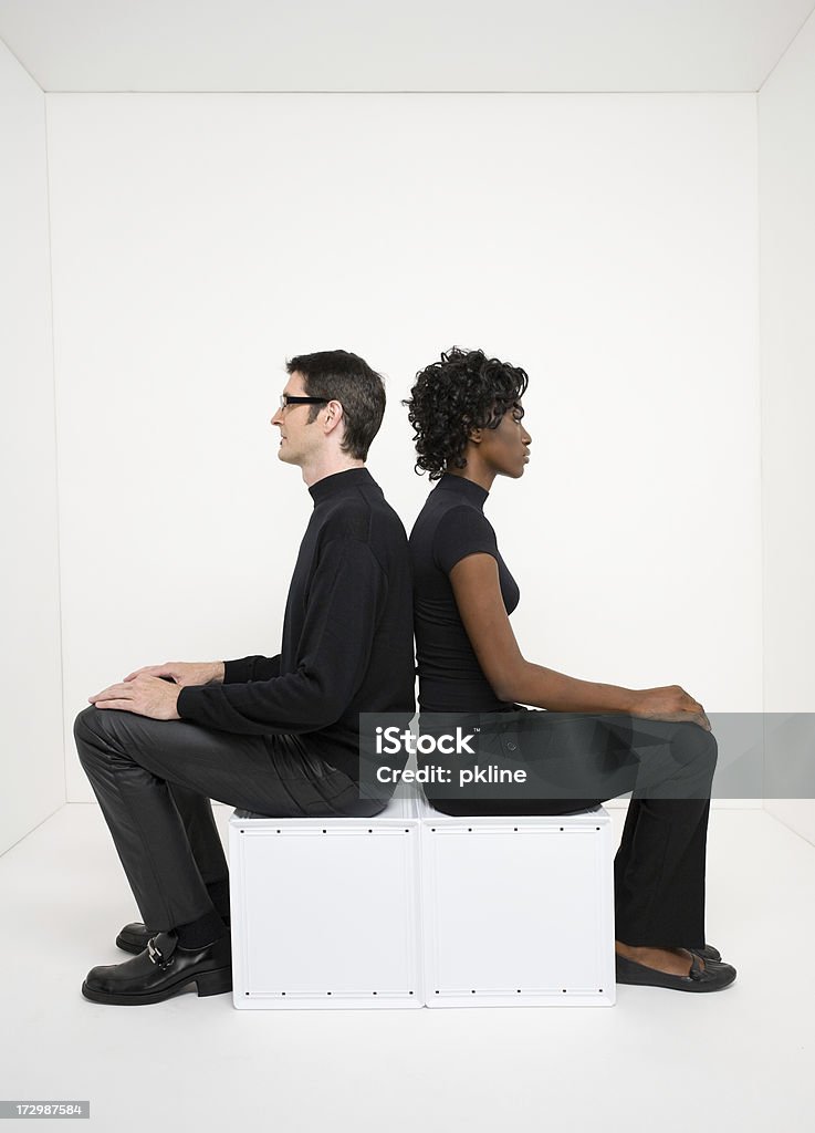 Young man and woman sitting in stark white room Young man and woman seated back to back in stark white room Back To Back Stock Photo