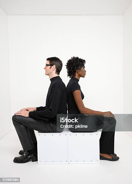 Young Man And Woman Sitting In Stark White Room Stock Photo - Download Image Now - Back To Back, Studio Shot, 20-24 Years