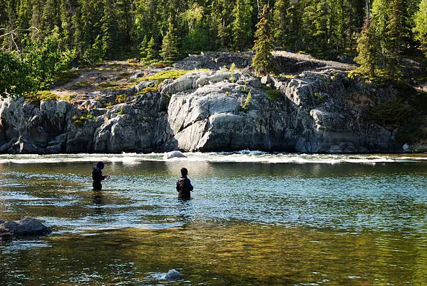Two people wade in an arctic river to fish.