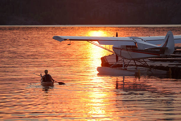 Kayak and Seaplane at sunset, Yellowknife, Northwest Territories, Canada. A kayaker and seaplane at sunset on Great Slave Lake at Yellowknife, Northwest Territories, Canada.  Water colour is golden as the lone paddler paddles under the wing of the docked seaplane.  There is a sun reflection on the water and good copy space. great slave lake stock pictures, royalty-free photos & images