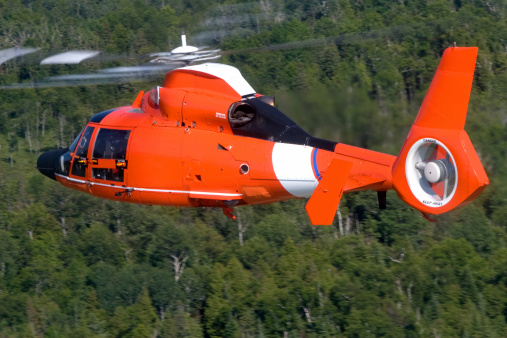 A Coast Guard Search and Rescue helicopter in flight above trees.