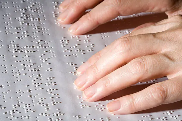 Extreme close up of female hands on a book written in Braille. Contrast lighting.