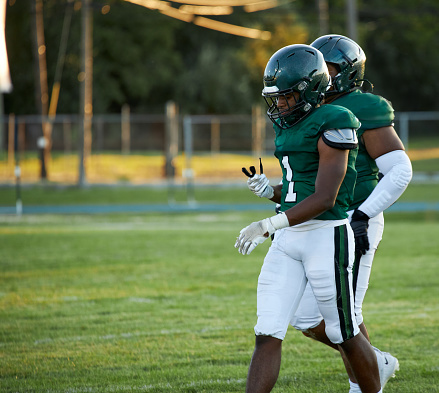 High school start football player walking off the field with another teammate