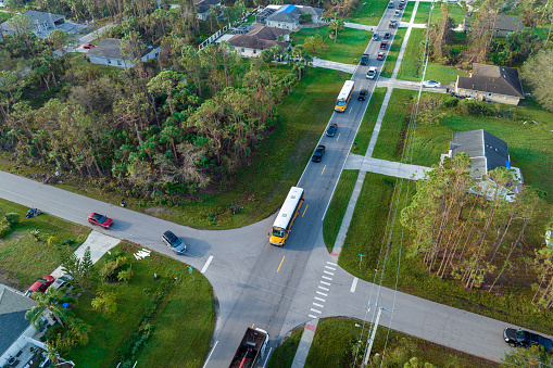 Aerial view of american yellow school bus picking up children at sidewalk bus stop for their lessongs in early morning. Public transportation in the USA.