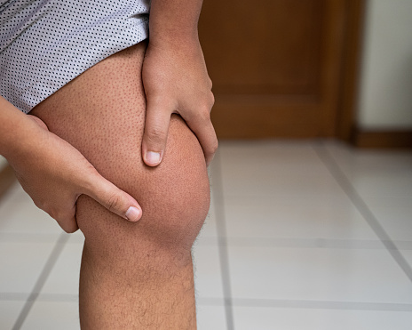 An unrecognizable man holds his swollen knee caused by a gout attack.