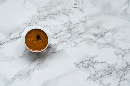 Top view of black coffee in white cup for breakfast on marble background with copy space