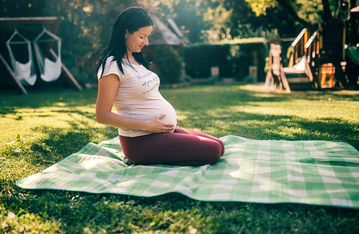 young pregnant woman is meditating in the yard