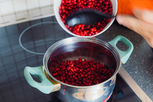 Female's hands cooking Swedish lingonberry jam in Scandinavian bright kitchen from berries harvested in the forest during autumn time