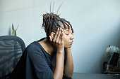 Young African-American woman with locs massaging her head with her hands at her desk in distress while sitting at her desk at her home office