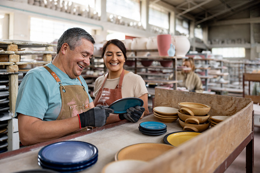 Happy Latin American employees working at a pottery factory doing quality control and smiling - production line concepts