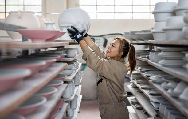 Latin American woman working at a pottery factory and putting a flower pot to on a shelf - production line concepts