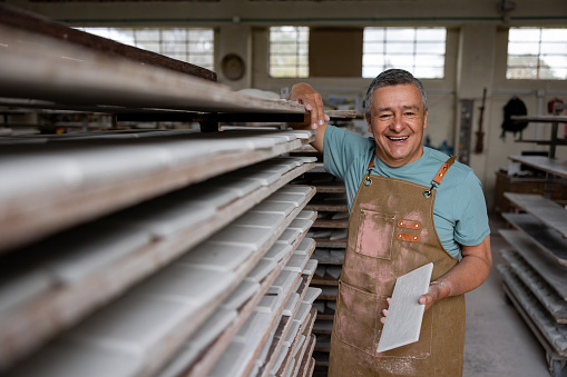 Portrait of a happy Latin American man working at a factory making a ceramic tiles and looking at the camera smiling - manufacturing concepts