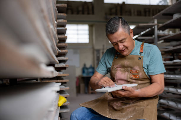 Happy Latin American employee working at a ceramics factory sanding a tile - manufacturing concepts