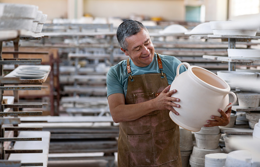 Happy Latin American man working at a pottery factory doing quality control on a crafts product - production line concepts