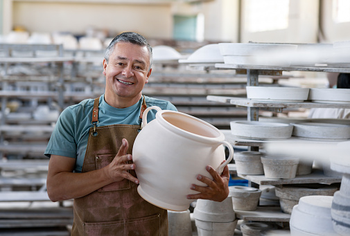 Portrait of a happy Latin American employee working at a pottery factory and looking at the camera smiling - manufacturing concepts
