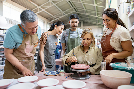 Woman teaching a group of Latin American students how to paint a plate at a pottery class