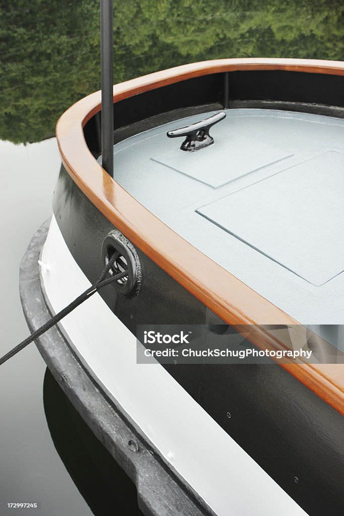 Boat Stern Hull Deck Mooring Cleat Classic steel hull boat with round stern and wood railing moored in still water. Close-up Stock Photo