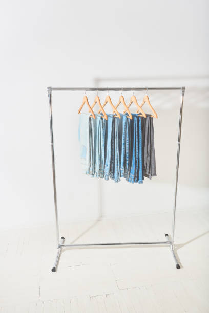 clothes rail with jeans of different colors hanging on hangers light minimalistic studio with a mobile clothes hanger. clothes rail with jeans of different colors hanging on hangers clothes hanger rod stock pictures, royalty-free photos & images