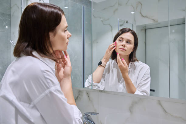 istock Young woman looking at her face in bathroom mirror 1729978044