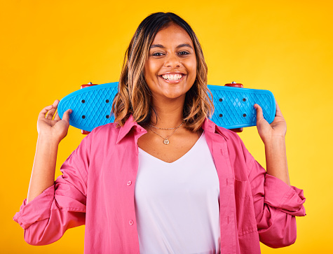 Woman, portrait and smiling with skateboard on yellow studio background, skater and excited. Cool, gen z face and happiness to skate, play and enjoy free time, in fashion clothes, outfit and stylish