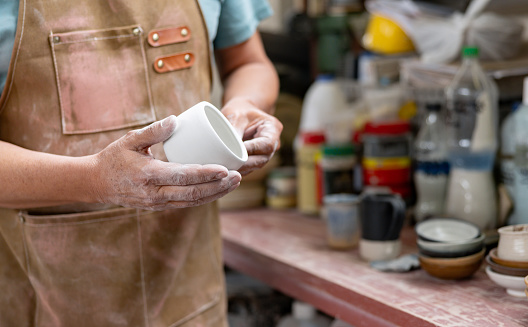Close-up on a potter holding a mug at a ceramics factory - manufacturing concepts