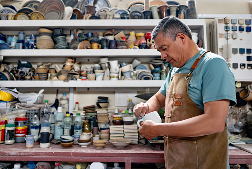 Mature Latin American man working at a ceramics factory sanding a mug - production line concepts