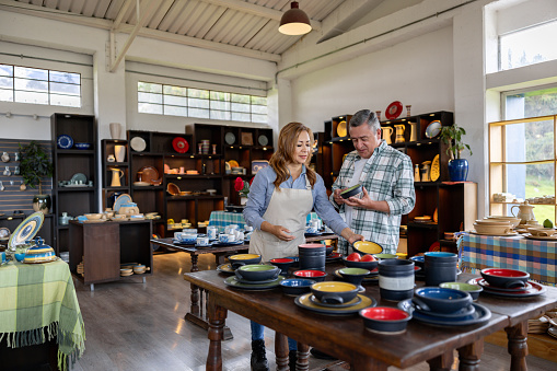 Happy Latin American man shopping at a pottery store with the help of a retail clerk - small business concepts