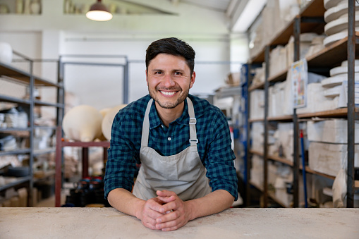 Portrait of a happy retail clerk working at a ceramics shop selling pottery and looking at the camera smiling