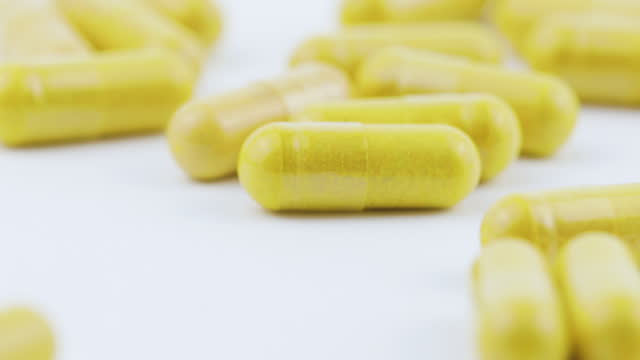 Capsules With Turmeric and Thistle Falling on White Background