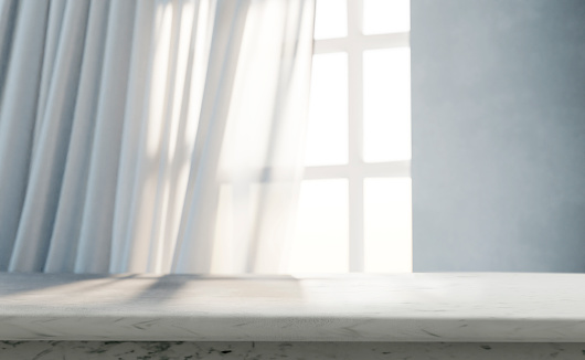 Empty marble table in front of window light and white curtains.
