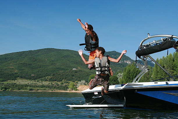 petit garçon sauter de bateau - life jacket little boys lake jumping photos et images de collection