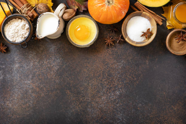 Homemade fall baking background with ingredients pumpkins, sugar, flour, nuts, eggs and spices on a dark stone table.