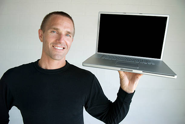 Smiling Young Man in Black Holding Blank Laptop Smiling young man with short hair in a long-sleeved black shirt holding an open laptop computer up with a smile crew cut stock pictures, royalty-free photos & images