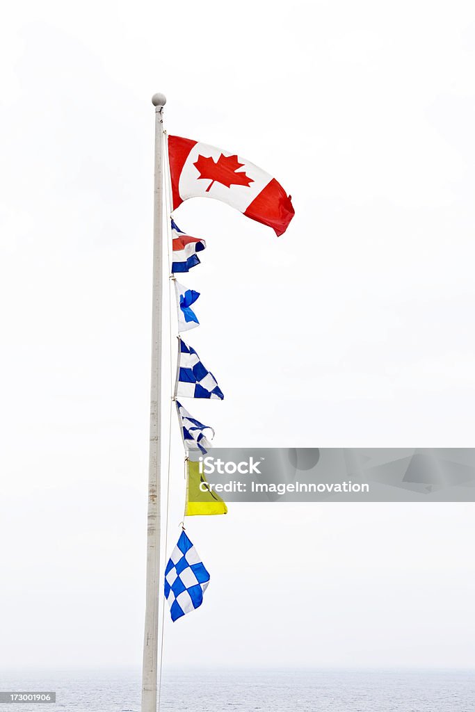 Maritime signal flags "A Canadian flag on a pole followed by a series of maritime signal flags on white, with ocean waters in the background." Nautical Flag Stock Photo