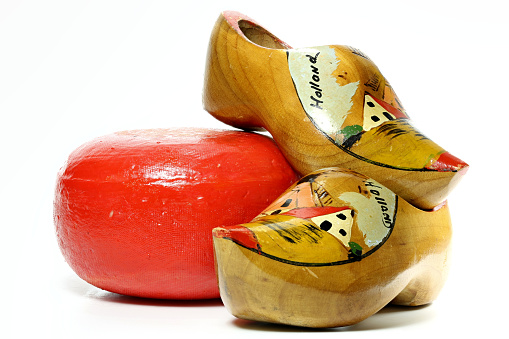 Row of pairs of used wooden shoes placed in line against a bright yellow wooden wall. Some wooden shoes are painted in traditional dutch pattern. Others are blank. The wooden shoes are part of the dutch culture in the Netherlands.