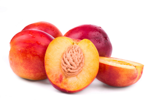 Fresh pink peaches in a wooden crate with leaves on a white background.