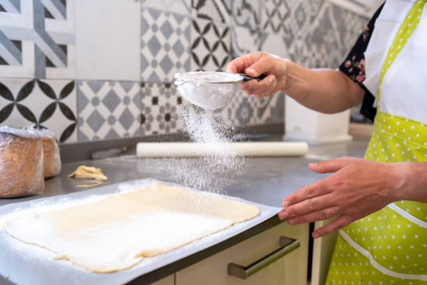 kobieta posypująca mąką ciasto w kuchni piekarni - flour sifter zdjęcia i obrazy z banku zdjęć